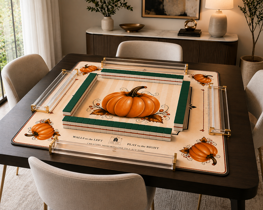 A decorative tabletop game board set displayed on a dark wood dining table in a styled dining room. The set includes a cream-colored board with orange pumpkins, green borders, and clear acrylic game pieces with gold-toned hardware.